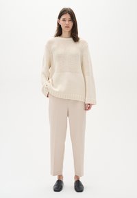Cremefarvet strikket sweater med løs pasform, ribbet kant og vertikale mønstre, parret med beige skræddersyede bukser og sorte slip-on sko.