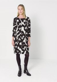 Czarna i biała sukienka w wzory z rękawami trzyczwartowymi, prostym krojem i okrągłym dekoltem, noszona z czarnymi rajstopami i botkami za kostkę.