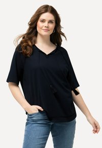 Top corto blu navy scuro con scollatura a V, frange decorative e cuciture texturizzate lungo l'orlo. Abbinato a jeans blu chiaro.
