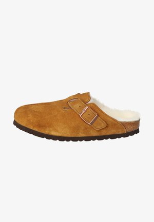 Clog maro din suede cu căptușeală din blană, cataramă metalică ajustabilă și talpă din cauciuc texturată. Design minimalist și formă rotunjită.