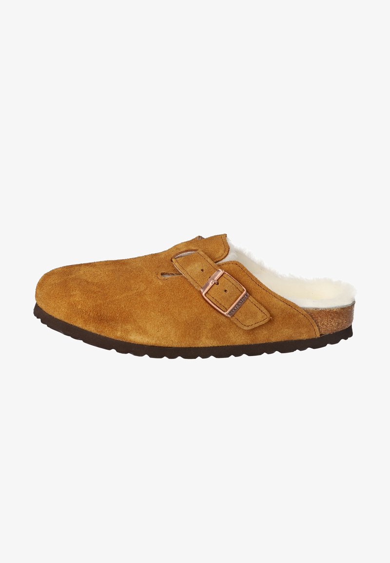 Tamanco de camurça castanho com forro de pelúcia, fivela metálica ajustável e sola de borracha texturizada. Design minimalista e forma arredondada.