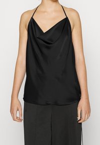 Haut en satin noir à col bénitier avec des fines bretelles ; texture lisse et design drapé, légèrement ample au niveau de l'ourlet. Porté avec un pantalon sombre.