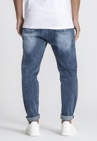 Jeans de mezclilla azul con un acabado ligeramente desvanecido, con puños enrollados y costuras en contraste. Combinados con zapatillas blancas y una camiseta blanca sencilla.