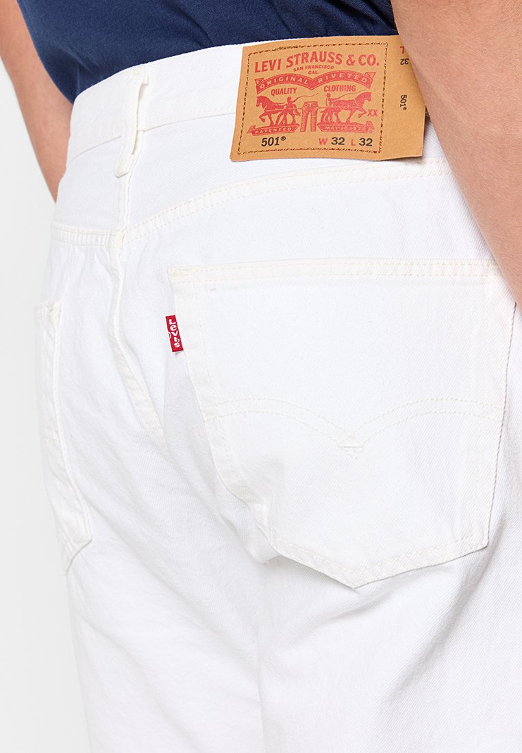 Weiße Denim-Jeans mit klassischem Design, rotem Levi's-Tag, gestickten Taschen und dezenten Details an den Gesäßtaschen.
