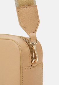 Beżowa torba ze strukturalną skórą w narożniku, z złotym zamkiem, złotym zapięciem oraz plecionym beżowym paskiem przymocowanym za pomocą skórzanej klapki.