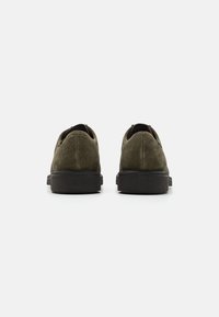 Zapatos de ante verde oliva con punta redonda, suela negra de goma de perfil bajo y tira en la parte trasera. Acabado texturizado con una silueta suave.