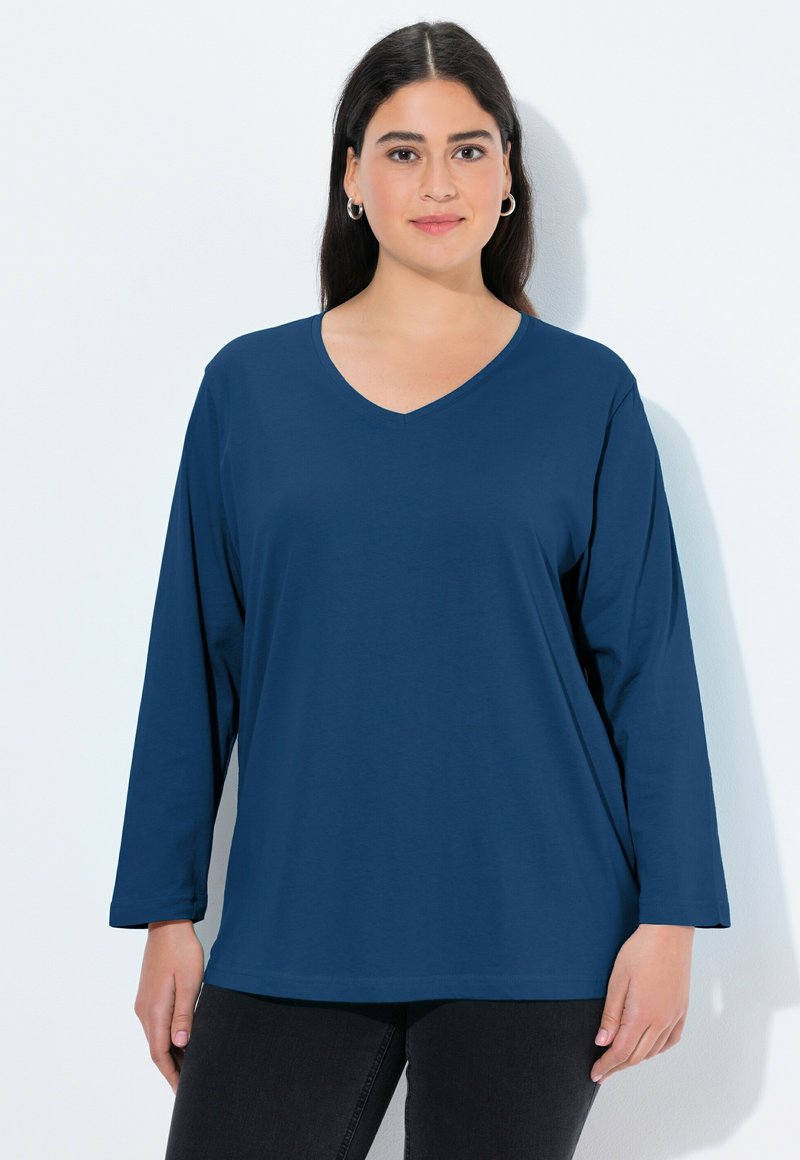 Marineblauwe longsleeve V-hals t-shirt van zachte stof, met een relaxte pasvorm en een gladde textuur, gedragen met zwarte broek.
