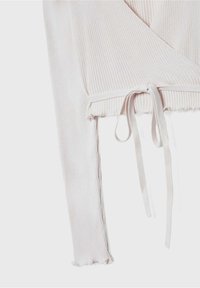 Haut côtelé rose clair à manches longues avec devant croisé et nœud noué à la taille, avec bordure ondulée sur les manches et l'ourlet.