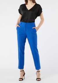Pantalon bleu sur mesure avec une texture lisse, doté d'un revers plié et de poches avant, associé à un haut noir à manches courtes.