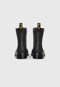 Μαύρες λάστιχες μπότες μέχρι τον αστράγαλο με γυαλιστερή φινίρισμα, στρογγυλή μύτη, χοντρή υφαντή σόλα και αντίθετους κίτρινους τράβηχτες στην πλάτη.