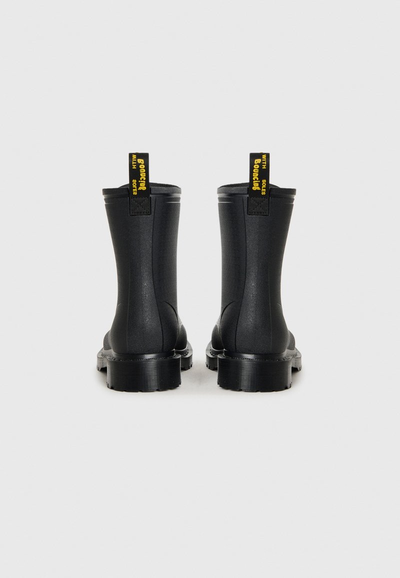 Schwarze Gummistiefel bis zum Knöchel mit glänzender Oberfläche, runder Zehenpartie, dicker strukturierten Sohle und kontrastierenden gelben Zuglaschen auf der Rückseite.