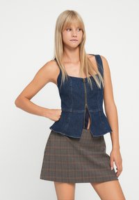 Denim peplum top met een vierkante halslijn en een rits aan de voorkant; heeft brede bandjes en een aansluitend lijfje. In combinatie met een geruite rok.