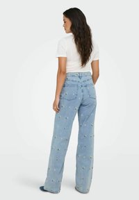 Lichtblauwe wijde jeans met bloemenborduursel, hoge taille en twee achterzakken. Gestyled met een aansluitend wit t-shirt.