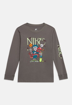 T-shirt gris à manches longues Nike avec un graphisme d’un squelette tenant un ballon de basket et une batte de cricket, enlacé par un serpent rouge avec des chauves-souris volant autour.