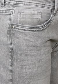Jeans in denim grigio con una tasca posteriore con cuciture visibili, tessuto testurizzato e una piccola decorazione in metallo.