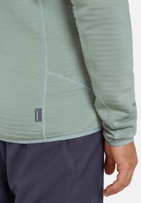 Lichtgroen longsleeve shirt met een gestructureerd oppervlak, naaddetails en een klein label. Gecombineerd met navykleurige stoffen broek.