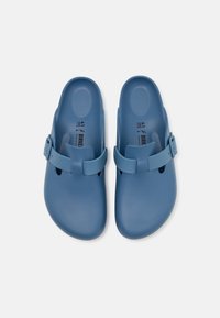 Blauwe plastic klompen met een gespband, voorzien van ventilatiegaten en een gladde textuur. Maat 41 staat binnenin aangegeven.