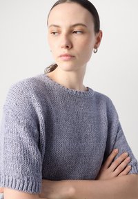 Világos lila kötött pulóver rövid ujjal, kerek nyakkivágással és texturált anyagból. A dizájn laza szabású, vastag bordás szegélyekkel rendelkezik.