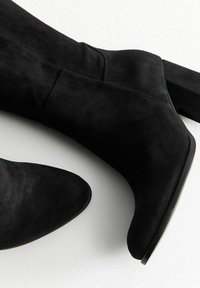Stivaletti neri in suede alla caviglia con punta affusolata e tacco spesso, caratterizzati da una texture liscia e un design minimalista.