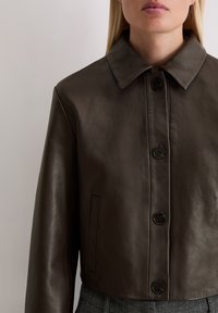 Braune Leder-Cropped-Jacke mit spitzem Kragen, Knopfverschluss und Seitentaschen. Glatte Textur und minimalistisches Design.