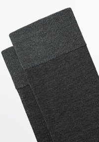 Calzini neri al ginocchio con una fascia superiore a coste testurizzata. Il tessuto appare morbido e senza cuciture, con un colore scuro uniforme in tutta la superficie.