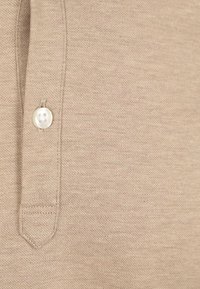 Beige polo shirt detail met een gestructureerde stof, een enkele ronde knop en een gestikte kraagplacket.