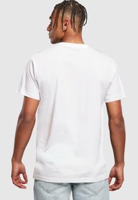 Weißes Baumwoll-T-Shirt mit klassischem Rundhalsausschnitt, kurzen Ärmeln und normaler Passform, von hinten mit minimalen Design-Details sichtbar.