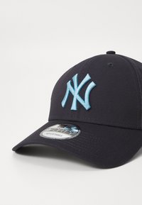 Mornarska kapa za bejzbol z bleščavim svetlo modrim vezenim logotipom "NY", strukturirano krošnjo, ukrivljenim vizorjem in nastavljivim trakom. Teksturirana tkanina.