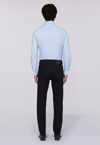 Ljusblå skjorta med lång ärm och knäppning framtill, ihop med svarta byxor. Skjortan har en slät textur; byxorna har en platt midja och bakfickor.