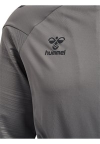 Camiseta deportiva gris con logo negro de Hummel que presenta una abeja estilizada en la parte superior del pecho y textura estampada en las mangas.