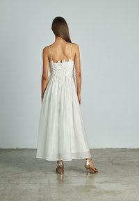 Witte maxi-jurk met kanten lijfje, verstelbare spaghettibandjes en een vloeiende rok. Draagt met metallic hoge hakken.