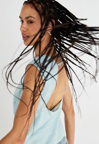 Un haut sans manches bleu clair avec une découpe profonde au dos, fabriqué en tissu doux, présentant une texture lisse et un design minimaliste.