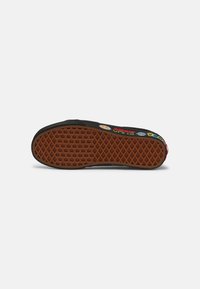 Black sneaker with a textured rubber sole, featuring colorful logos and accents. The sole has a honeycomb pattern for traction.