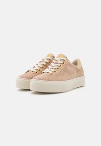 Beige Wildledersneaker mit einer dicken weißen Sohle, goldenen Ösen, cremefarbenen Schnürsenkeln und einem kontrastierenden, hellen Tan-Fersenelement.