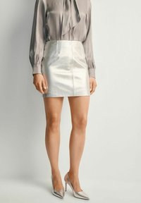 Metaliczna srebrna mini spódnica w połączeniu z jasnoszaryą bluzką z kokardą, uzupełniona metalicznymi szpilkami.