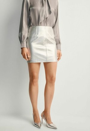 Metaliczna srebrna mini spódnica w połączeniu z jasnoszaryą bluzką z kokardą, uzupełniona metalicznymi szpilkami.