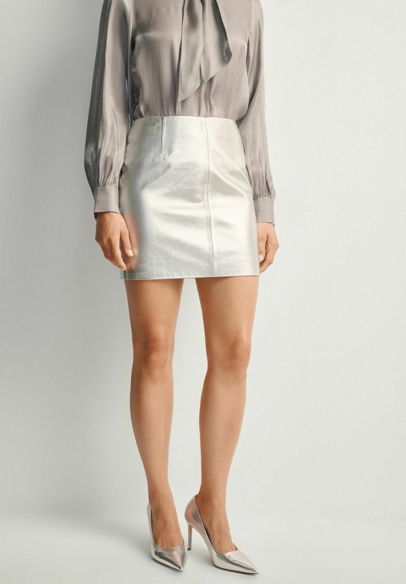 Metaliczna srebrna mini spódnica w połączeniu z jasnoszaryą bluzką z kokardą, uzupełniona metalicznymi szpilkami.