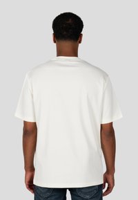 Krótki rękaw, biały T-shirt o luźnym kroju, okrągłym dekolcie i bocznych rozcięciach; gładki bawełniany materiał bez widocznych wzorów czy akcentów.