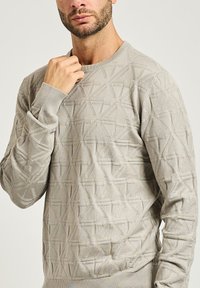 Maglione lavorato a maglia grigio chiaro con un motivo geometrico testurizzato, collo rotondo e polsini e orlo a costine. Realizzato in materiale morbido.