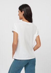 T-shirt en coton blanc à manches courtes retroussées, avec un col rond et une coupe décontractée. Accompagné d'un jean en denim bleu.