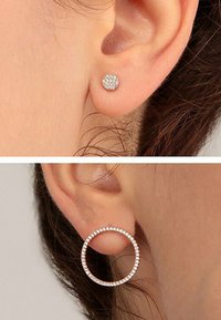 Två par örhängen: ett par har små runda, klara rhinstenar infästa i metall, och det andra har en större cirkulär design med rhinstenar.