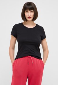 T-shirt noir à manches courtes avec un col rond, associé à un pantalon de jogging rose avec taille élastique et poches latérales.