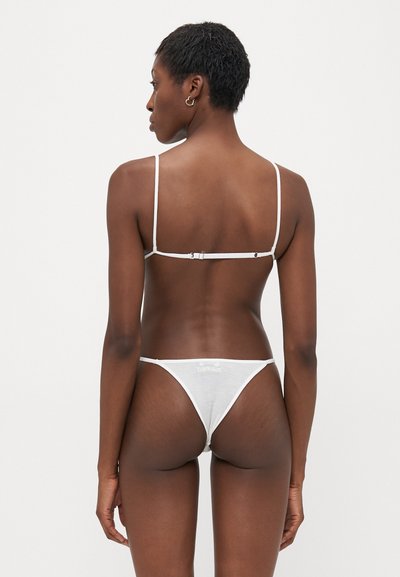 Balta mežģīņu bralette ar regulējamiem siksniņām, ar āķa aizdari un atbilstošām biksītēm. Iezīmējas ar delikātu tekstūru un minimālistisku dizainu.