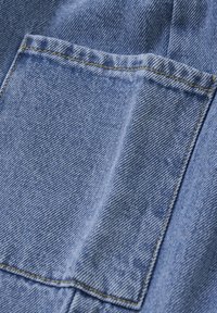 Denimtyg i en ljusblå nyans med en stor sidopocket. Synlig gul sömnad lyfter fram fickan och kanterna.