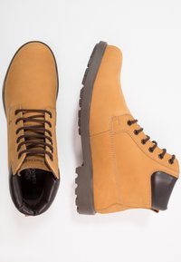 Bottes de randonnée en cuir marron avec une finition lisse, une semelle en caoutchouc robuste et un panneau de talon marron foncé renforcé. Six œillets avec lacets.