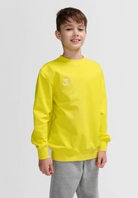 Klart gul sweatshirt gjord av bomull, med en ribbad rundhalssdesign och en liten vit logotyp. Matchad med grå sweatpants.