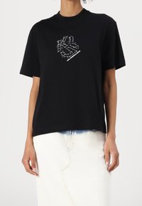 Henkilö, jolla on päällään musta T-paita valkoisella piikkilankalogolla ja "Karl Lagerfeld Jeans" -teksti, yhdistettynä valkoiseen hameeseen, jossa on sinisiä yksityiskohtia.