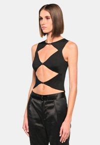 Black cropped top with cut-out design, featuring angular shapes and gold hardware accents. Paired with high-waisted black satin pants.