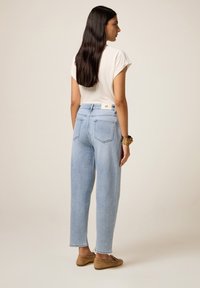 Jeans de tiro alto en azul claro con corte recto y dos bolsillos traseros, combinados con una blusa de mangas cortas en color crema y zapatos marrones.