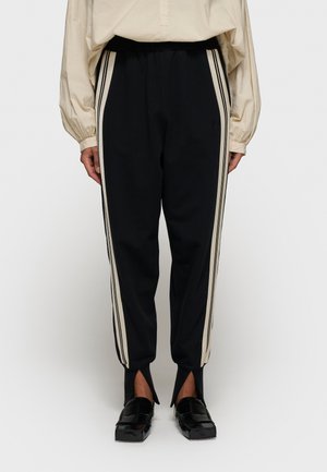 Pantaloni della tuta neri con strisce laterali beige, vestibilità affusolata, vita elastica e spacchi aperti all'orlo. Materiale misto cotone.